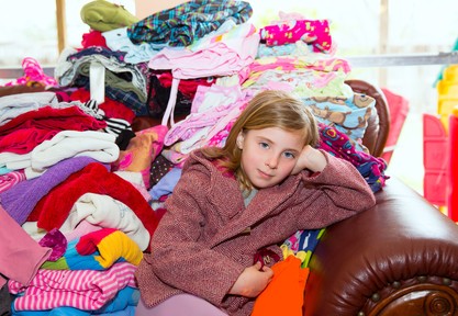 Blond kid girl sitting on a messy clothes sofa